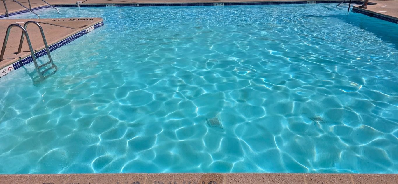 Clear blue water in a swimming pool, with splashes of sunlight reflecting on the surface.